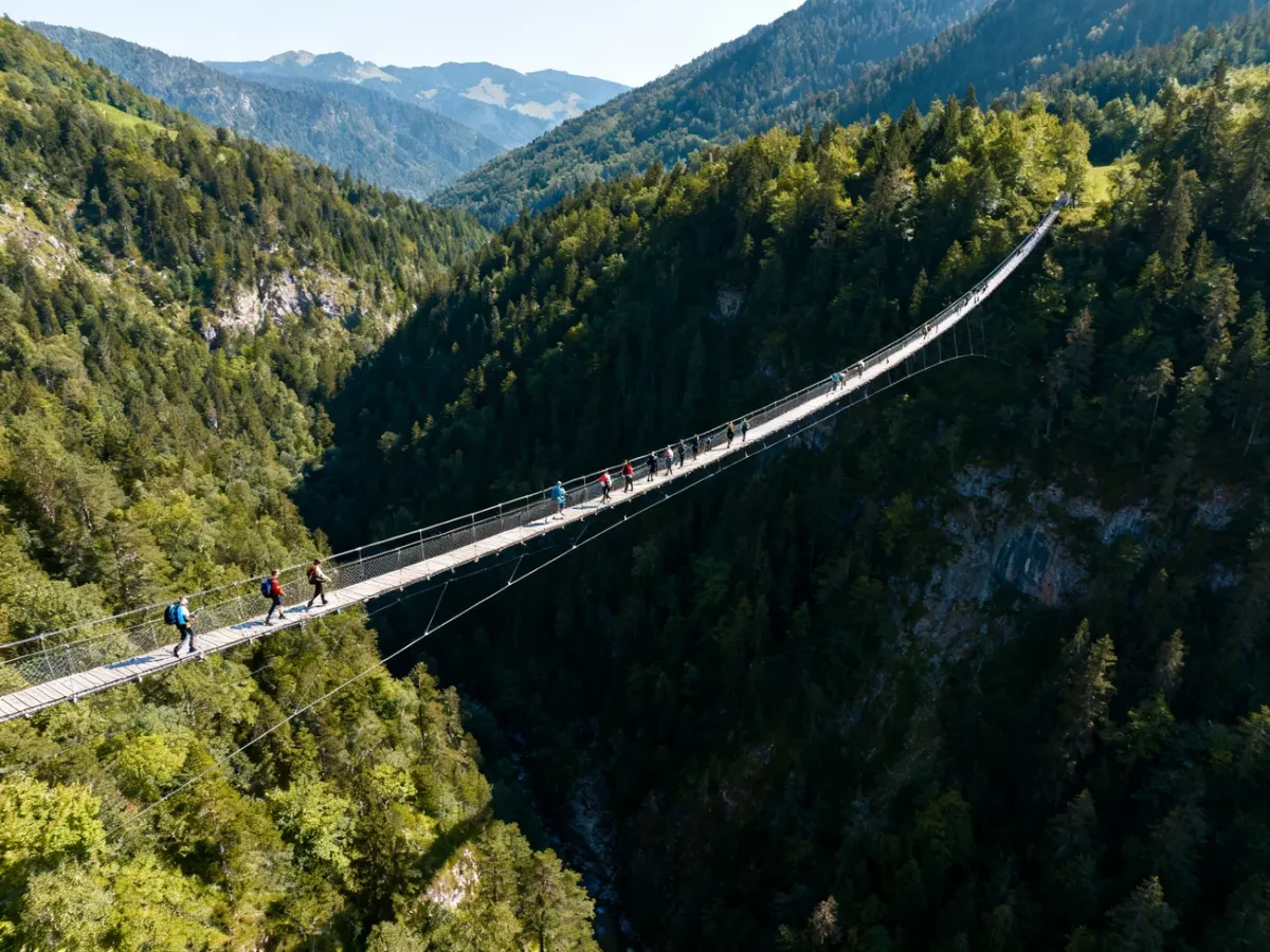 Turyści przechodzący przez długi most Sky Bridge 721 nad górską doliną